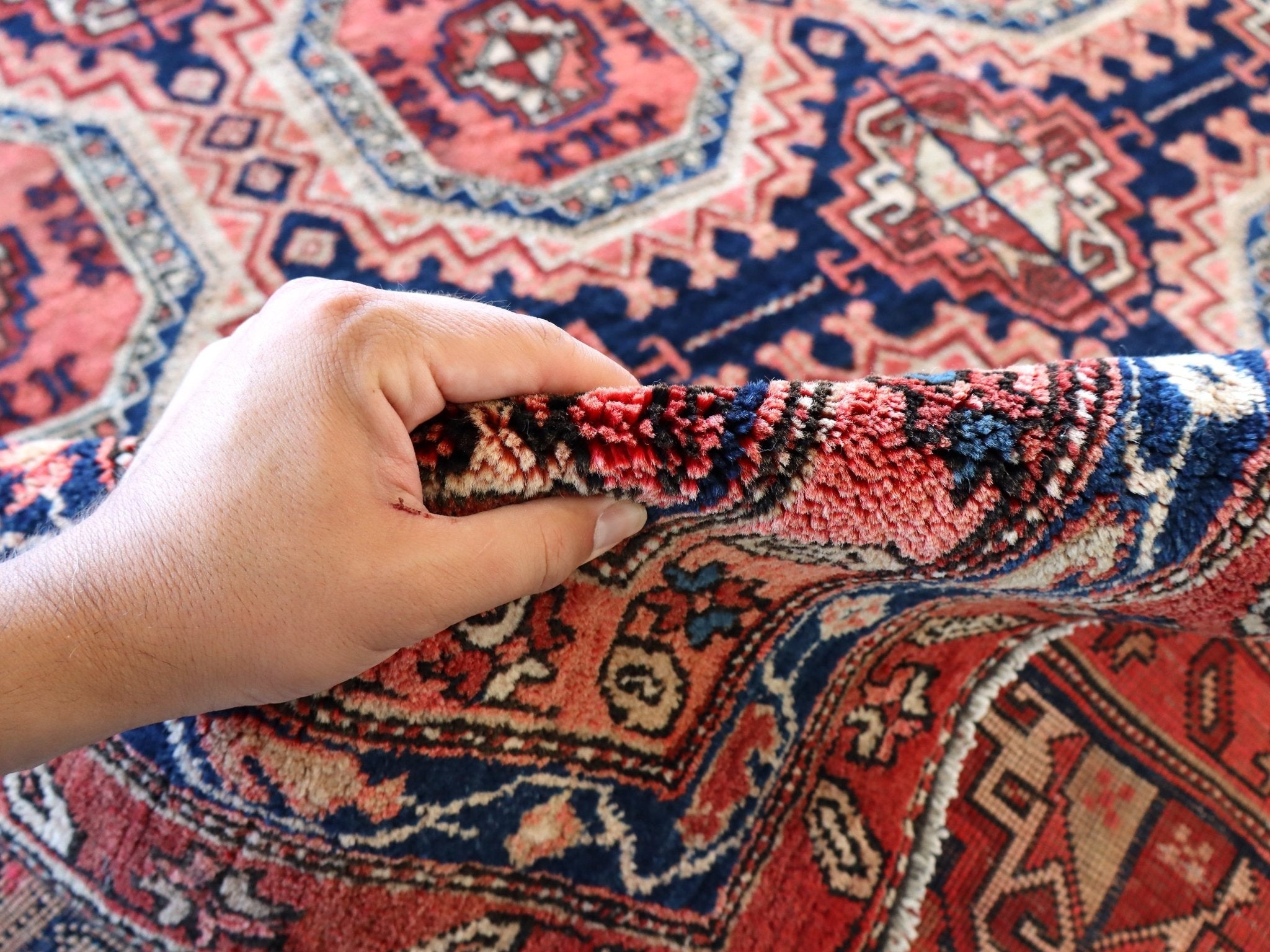 Persian runner rug edge with hand gripping short fringe; red navy and cream pattern
