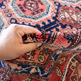 Persian runner rug edge with hand gripping short fringe; red navy and cream pattern