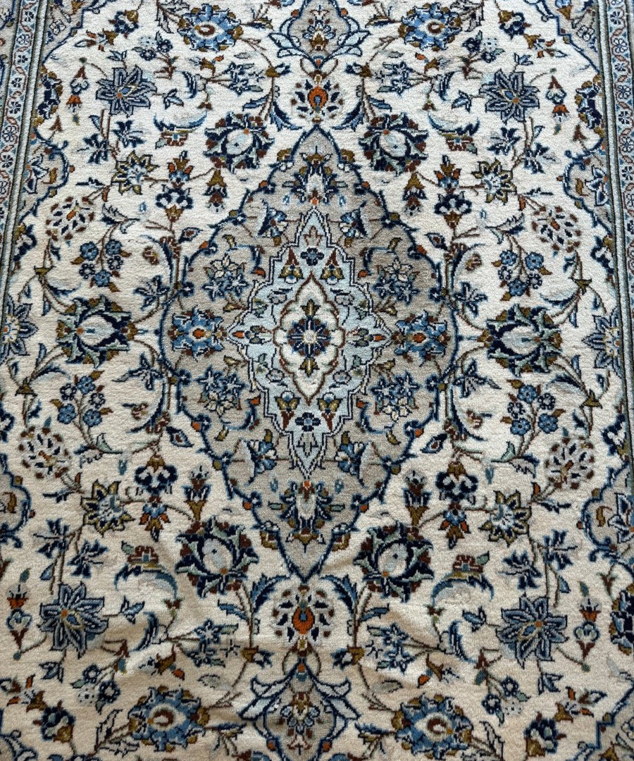 Close-up of ivory rug with intricate blue floral vine and medallion detailing