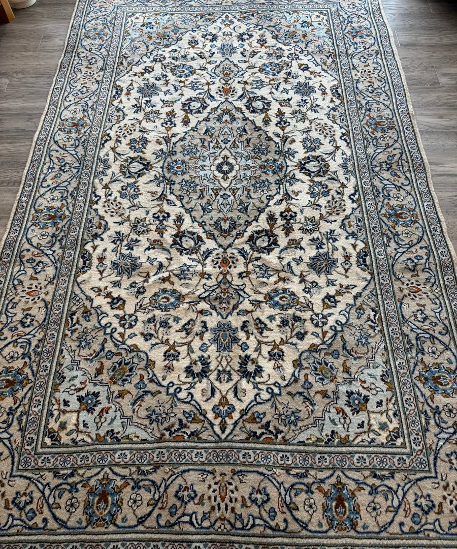 Ivory Kashan-style rug with blue floral medallion and ornate border pattern