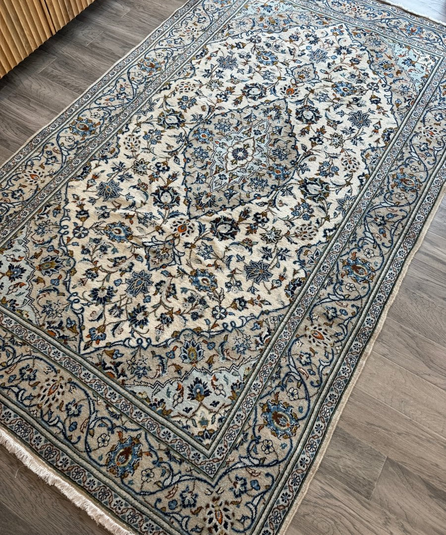 Corner view of ivory Kashan-style rug with blue floral medallion center
