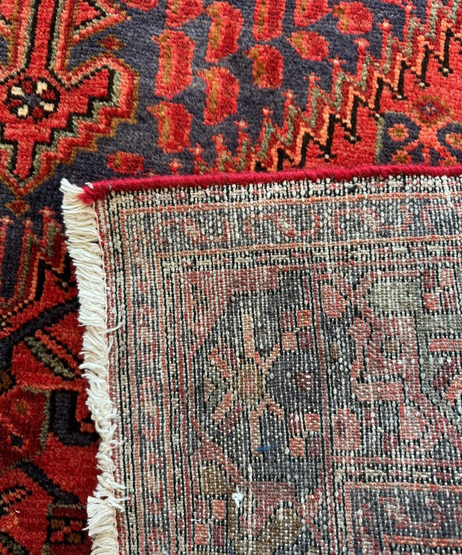 Red Persian-style rug corner close-up with fringed edge and woven texture