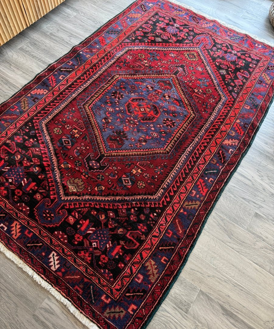 Red rug with central navy medallion, geometric motifs, and blue border details.