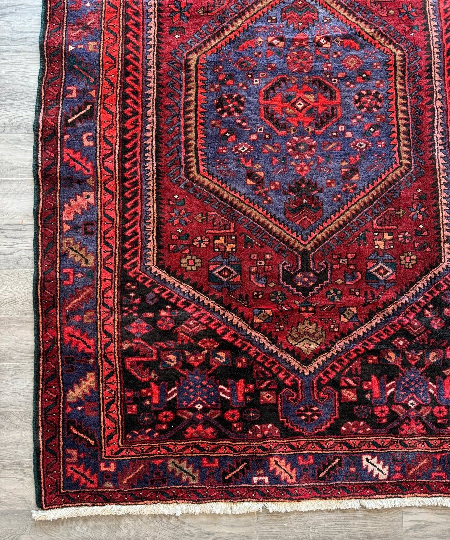 Red rug with central navy medallion, corner ornaments, and blue trim.