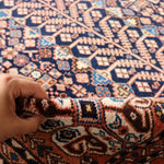 Hand pressing Persian-style rug fibers; navy and rust geometric pattern close-up.