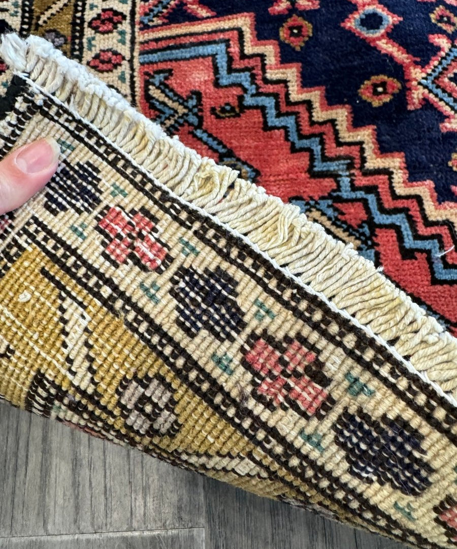 Close-up of rug edge with fringed border and geometric pattern in red, navy, cream, gold