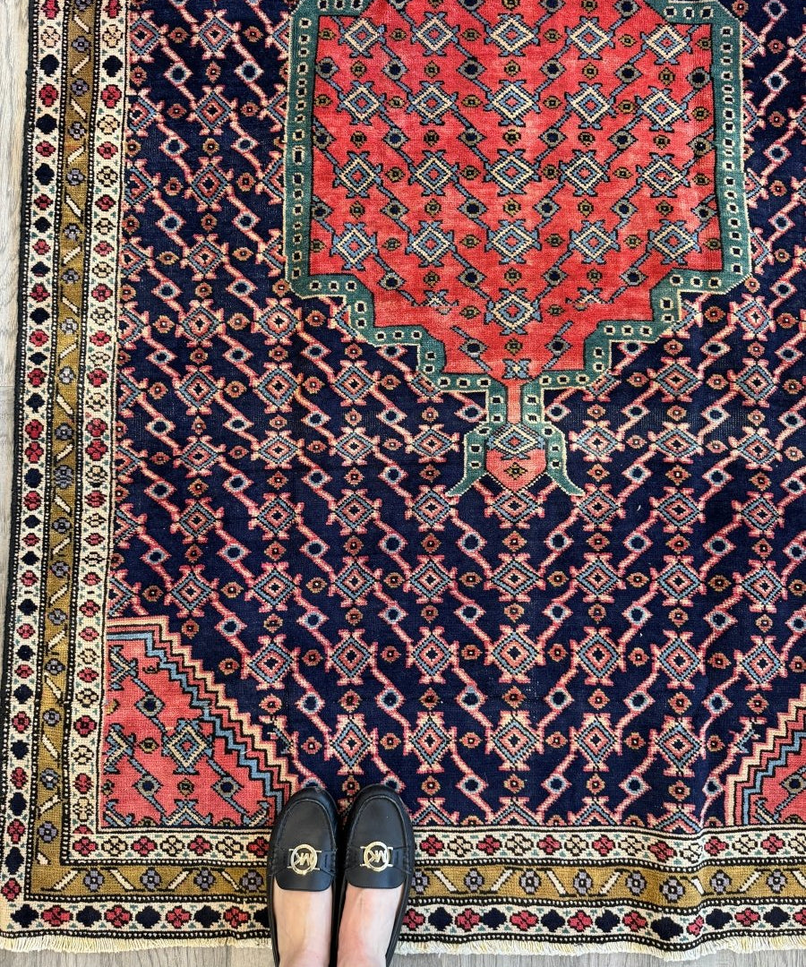 Persian-style rug with red center medallion, navy and teal geometric pattern, fringed border