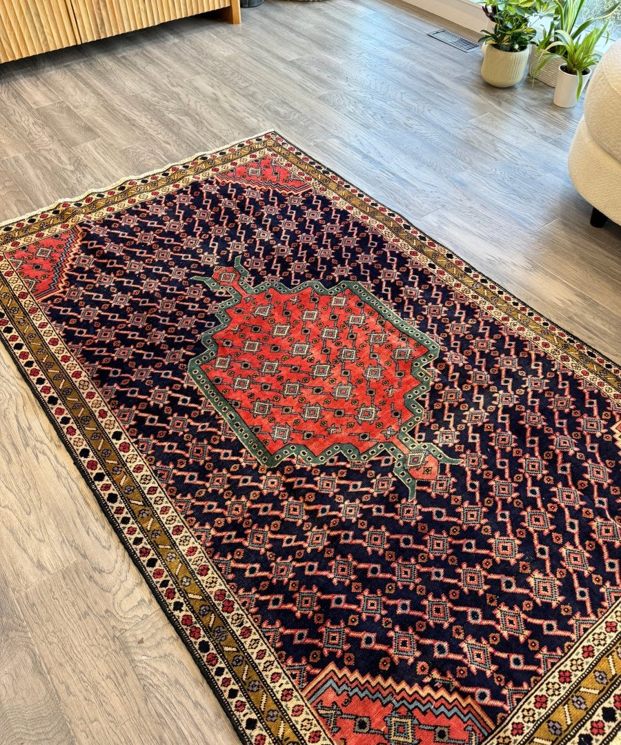 Persian-style rug with red medallion, navy field, multicolor border, angled view