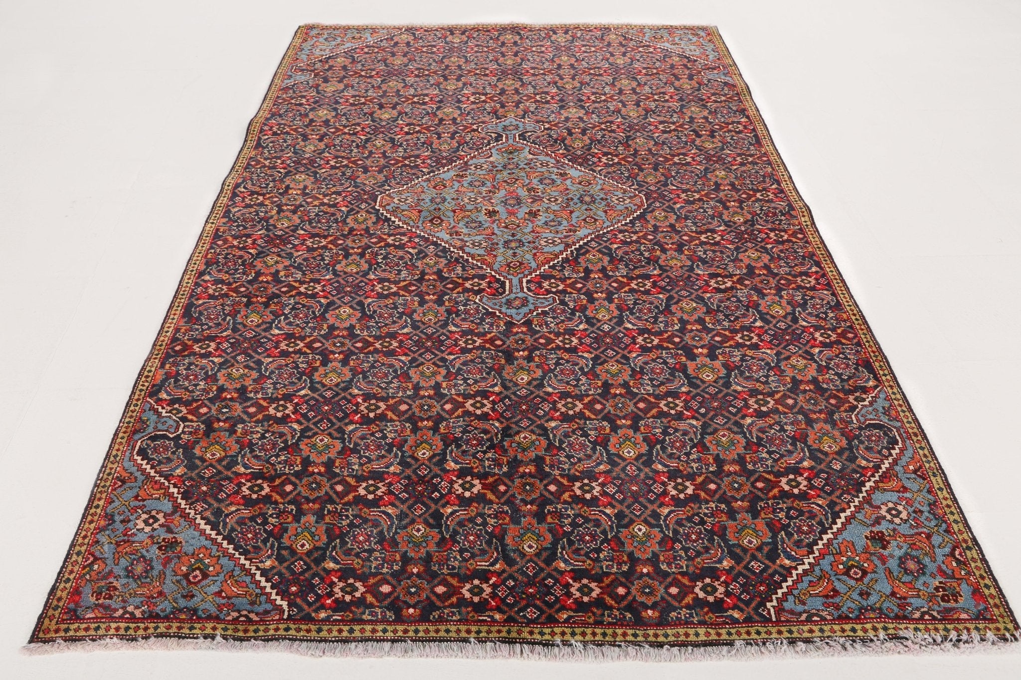 Full Persian rug view with dense red-orange, navy, and teal geometric motif field