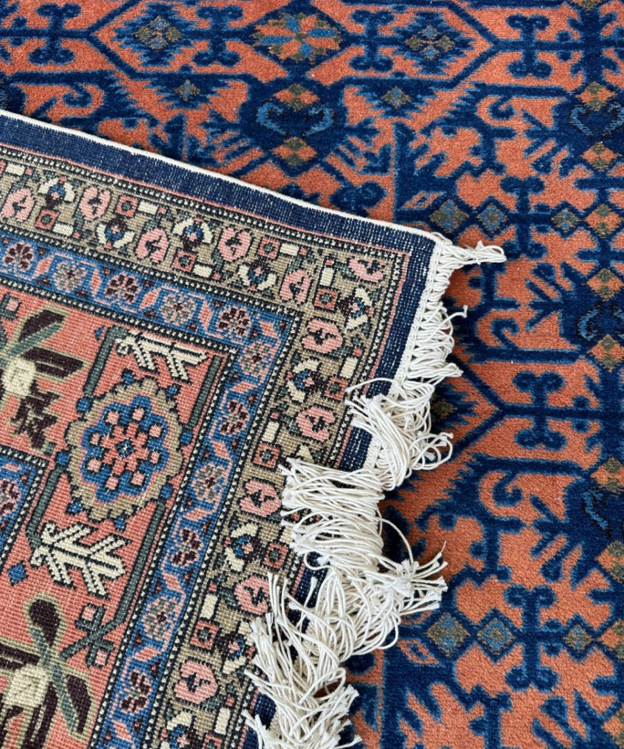 Persian Ardabil rug corner close-up, blue geometric pattern with orange ground and fringe