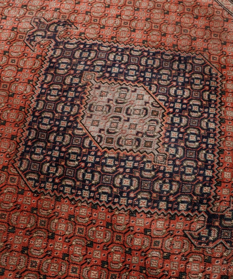 Persian Ardabil-style rug close-up, rust field with geometric medallion and navy motifs