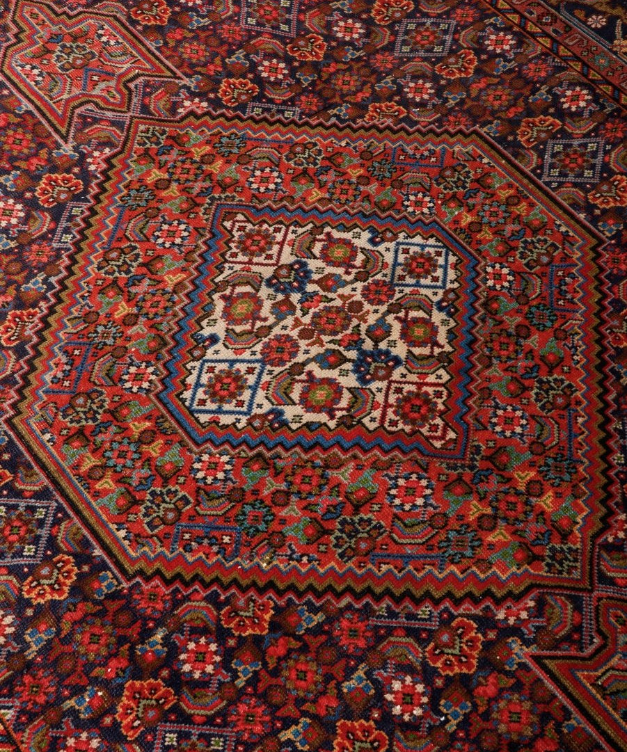 Persian Ardabil-style rug close-up with red, teal, and cream geometric motifs and border