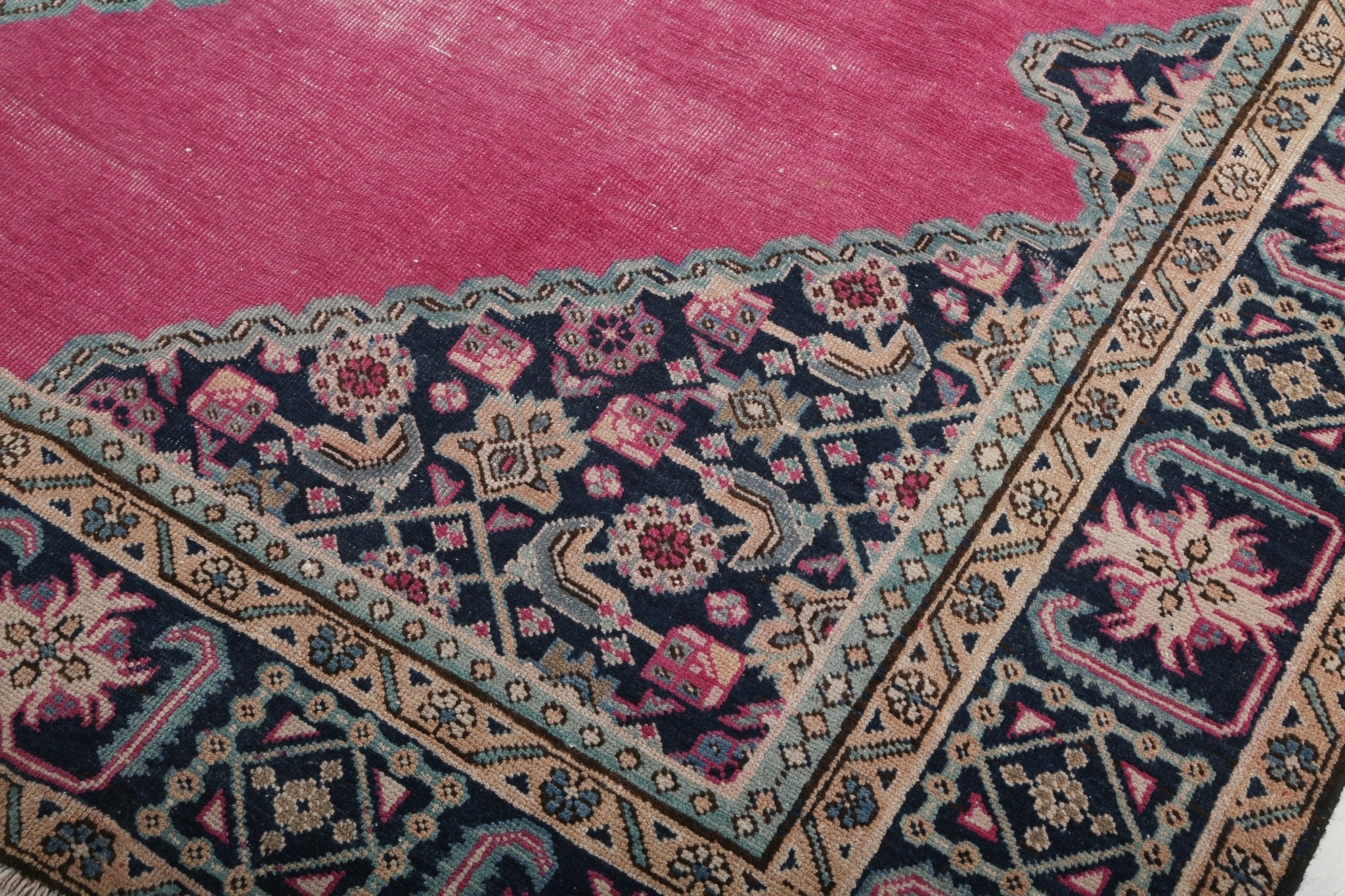 Persian rug close-up of navy floral corner pattern on pink field with border trim