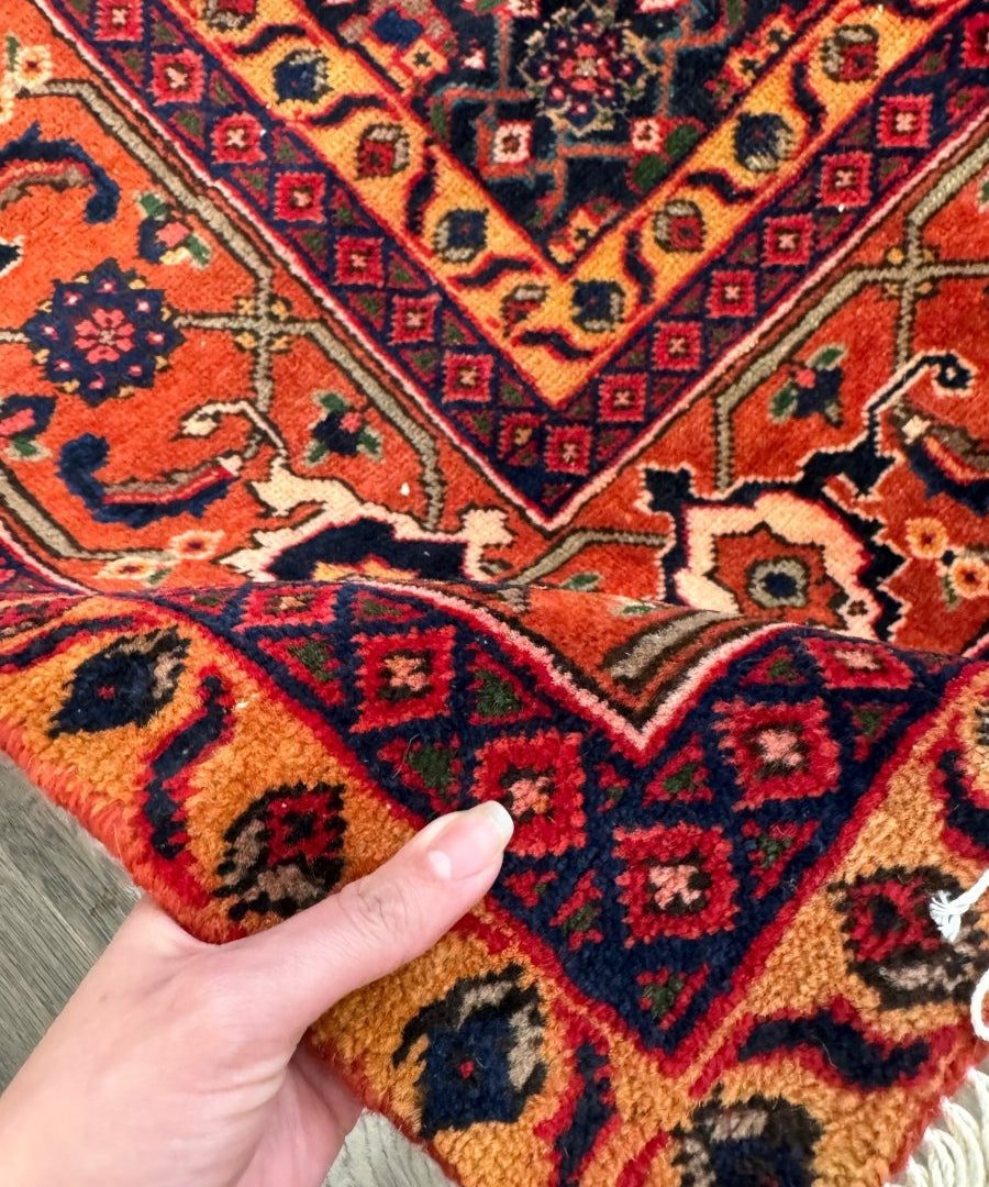 Close-up Persian Ardabil rug: red, navy, and gold geometric motifs with short cream fringe