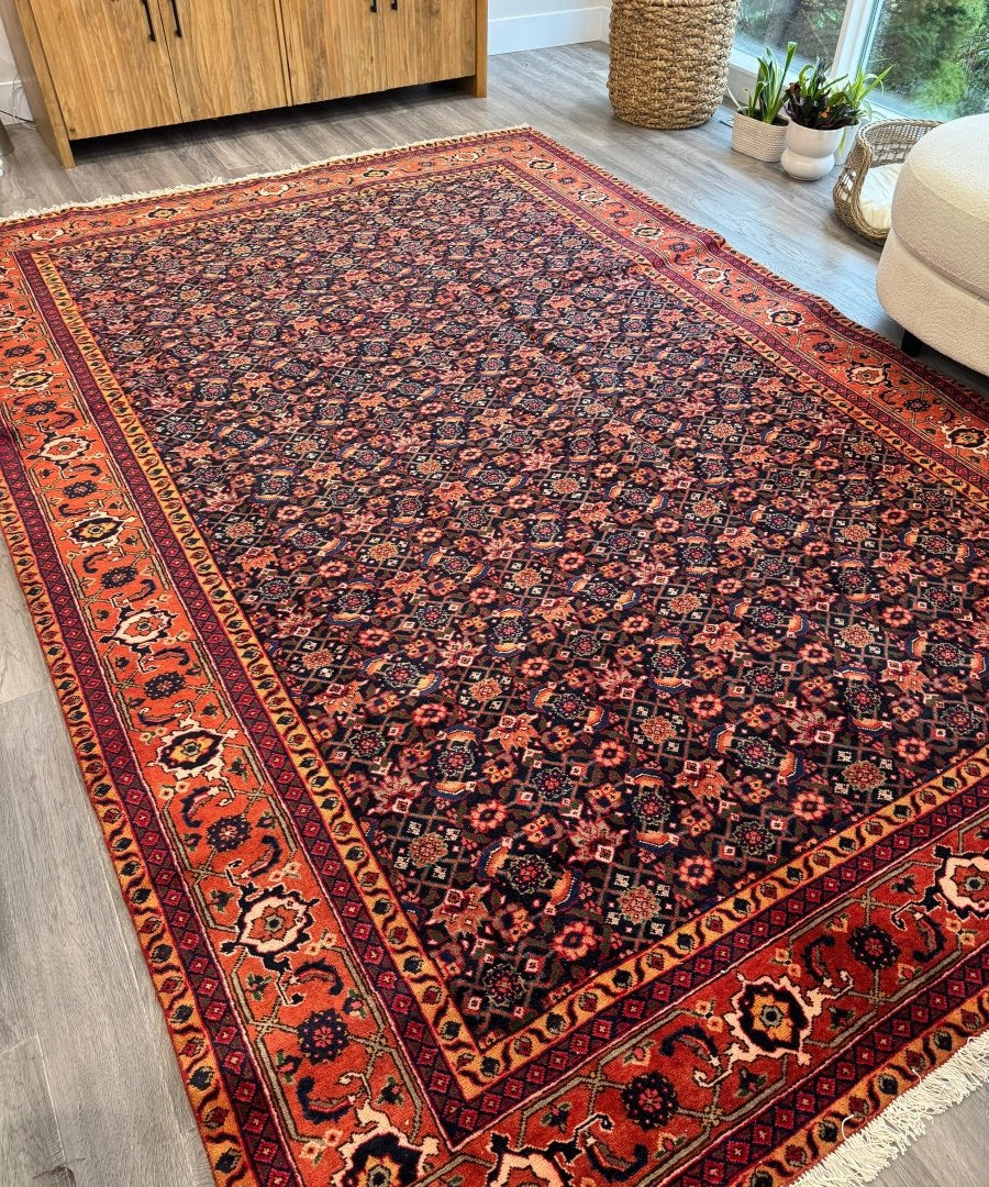 Persian Ardabil rug with rust border and dense navy-blue geometric pattern, light fringe