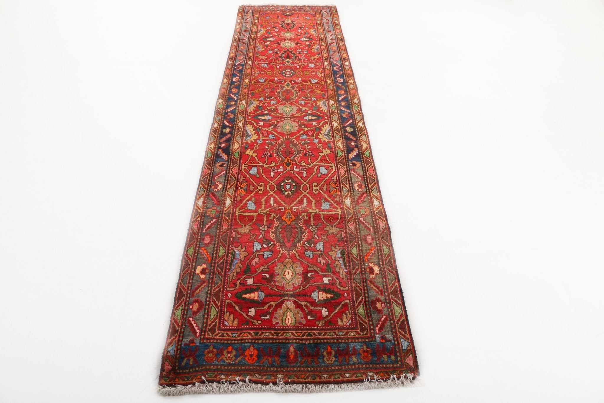 Red runner rug with symmetrical motifs, navy border, and short fringe along bottom