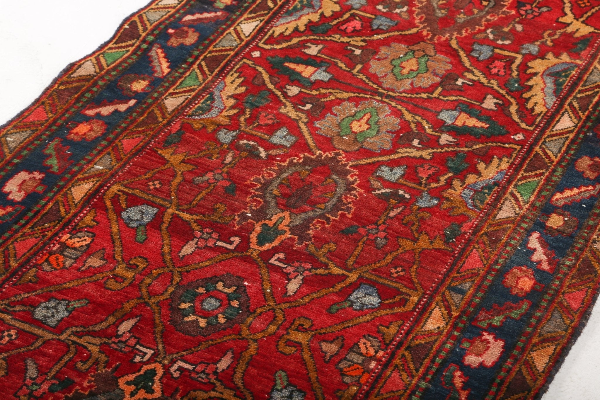 Runner rug surface detail with red field, navy outlines, and green accents