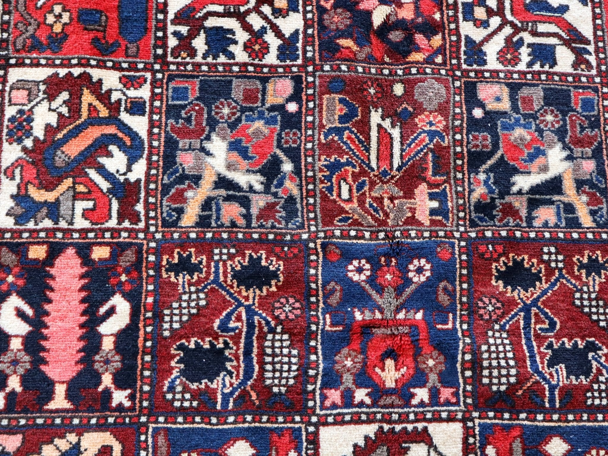 Persian rug detail of blue and red motifs with cream ground and small diamond borders