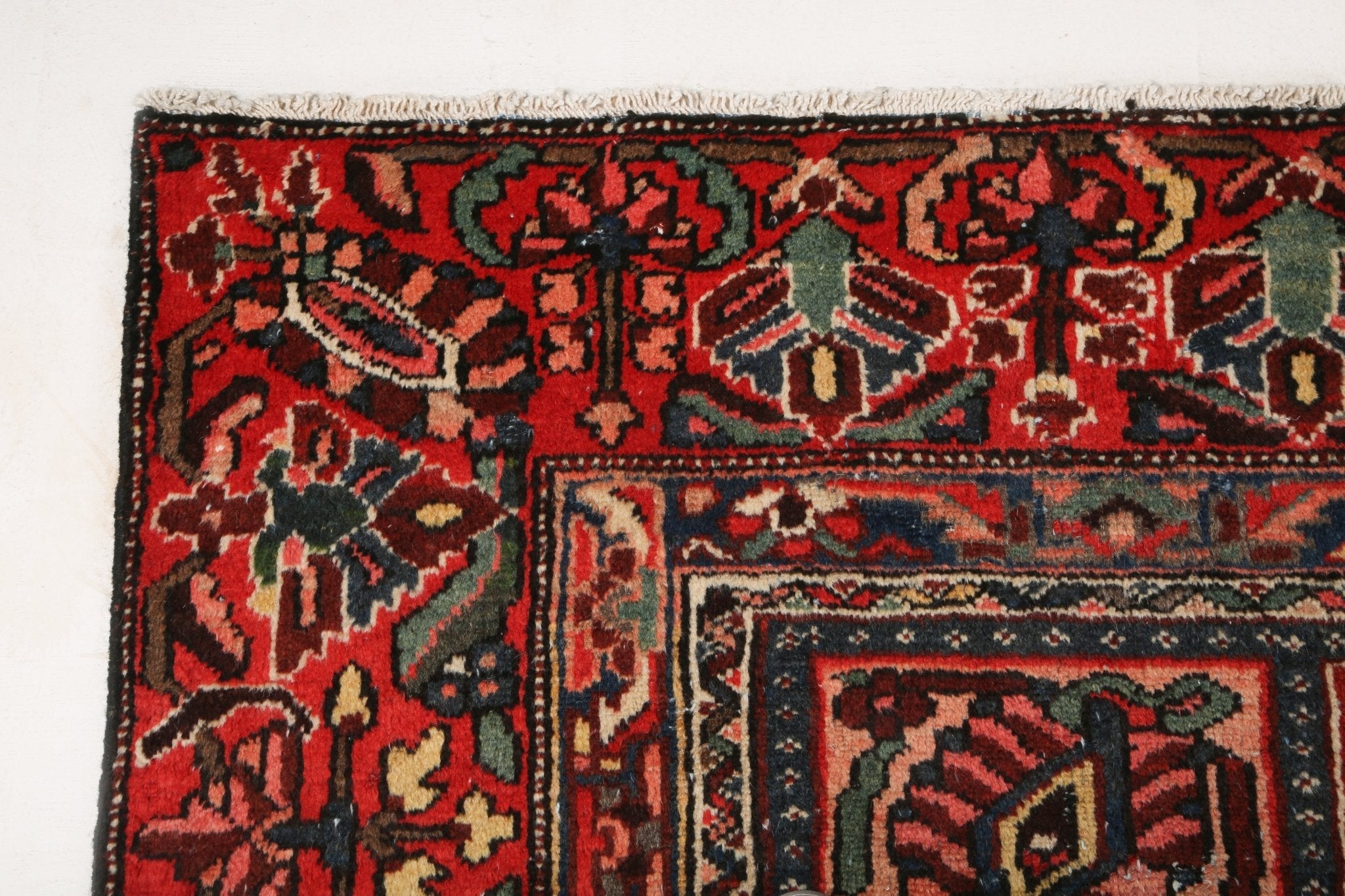 Rug close-up showing red ground, navy and cream motifs, and ornate border details.