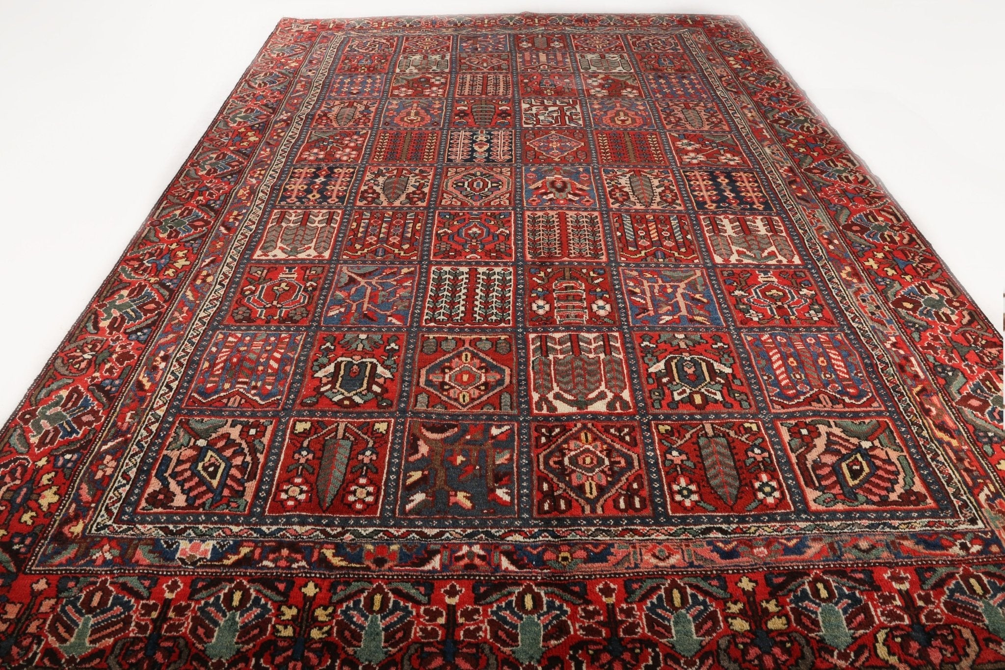 Persian-style rug laid flat with red medallion layout, blue accents, and patterned border.
