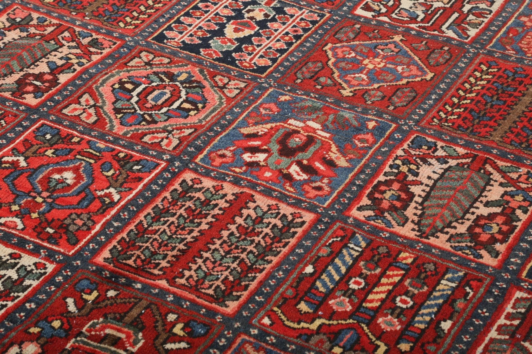 Rug surface view with red, blue, and cream geometric panels and repeating small motifs.