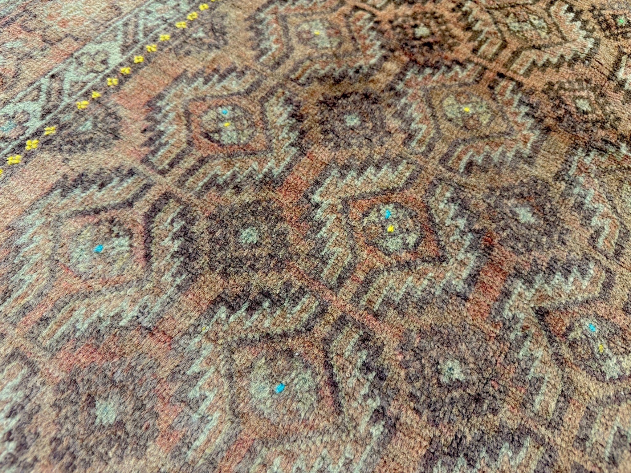 Persian Baluch rug texture detail with faded turquoise, rust, and tan geometric motifs and dots.