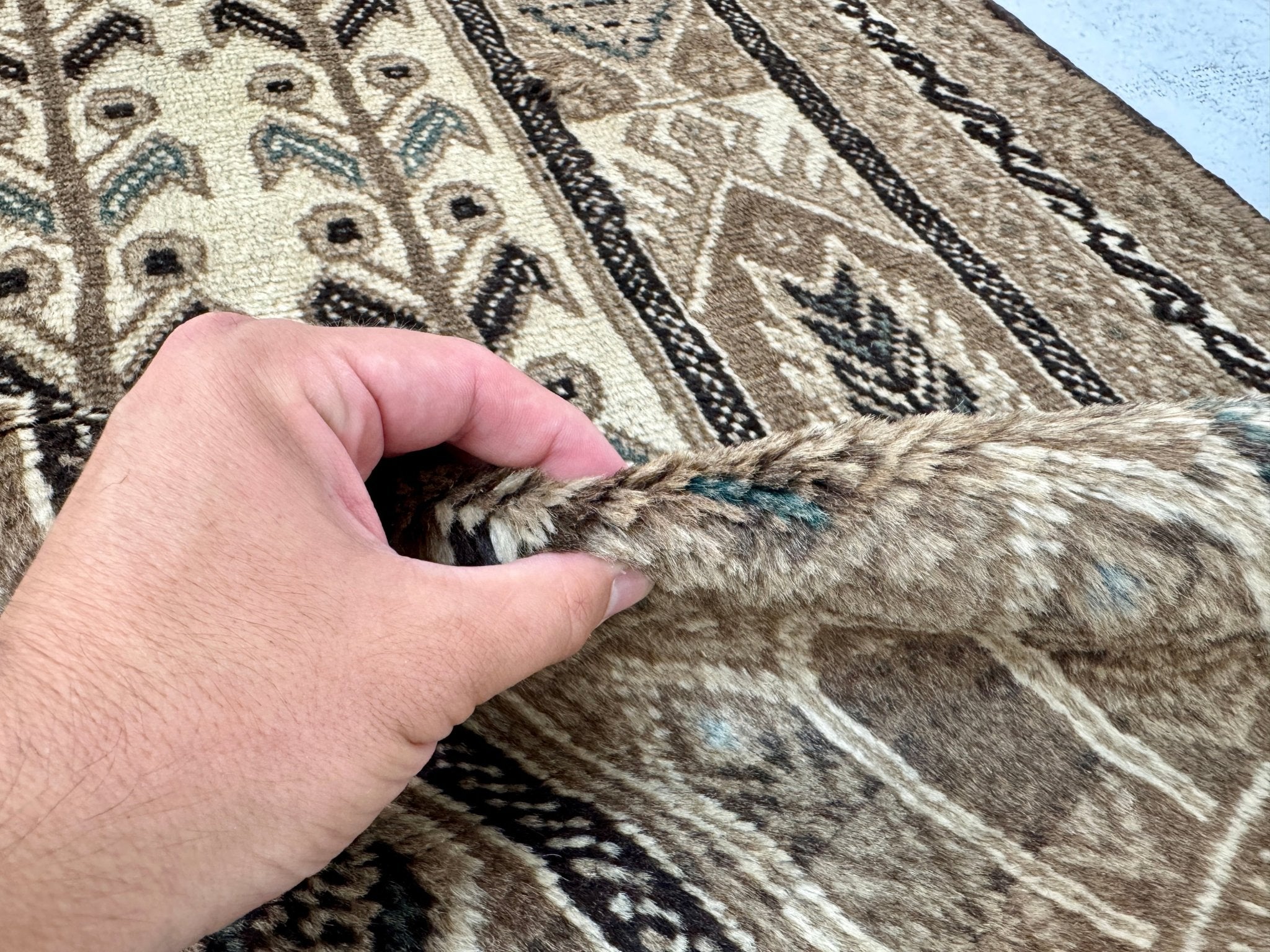 Persian Baluch rug corner detail showing hand lifting the textured pile
