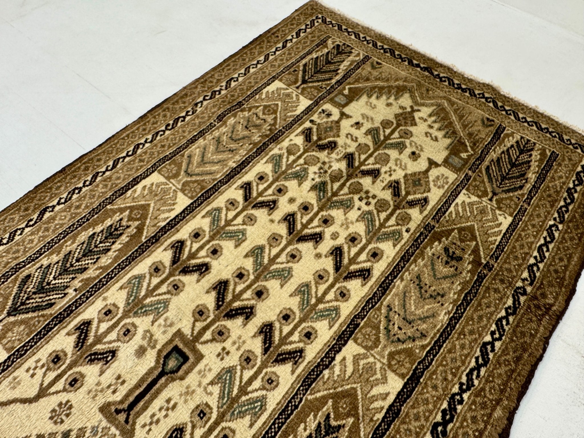 Close-up of Persian Baluch rug pattern with beige field, olive accents, and dark trim