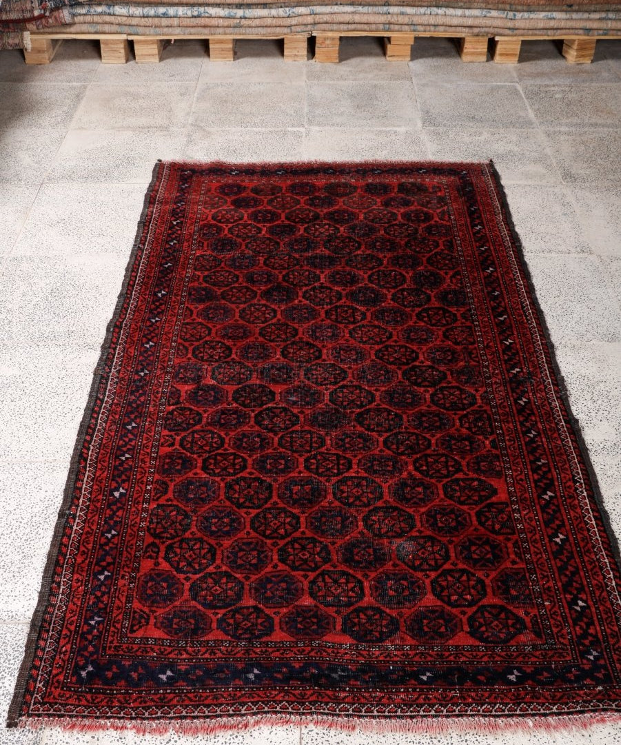 Persian Baluch rug laid flat on tile floor, red center with dark geometric motifs