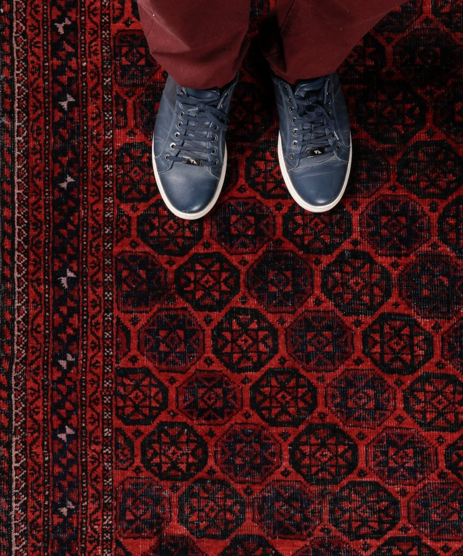 Persian Baluch rug with red and black pattern, worn by shoes standing on the weave