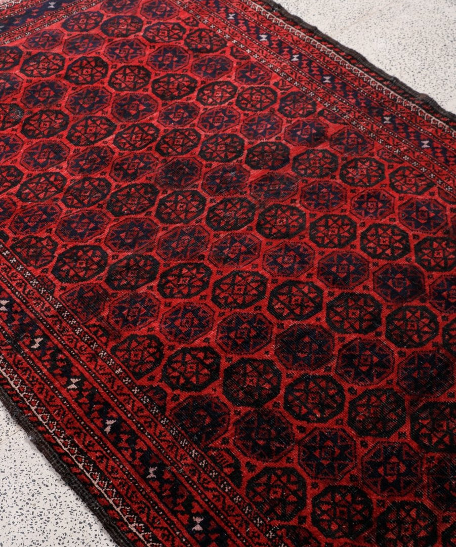 Close-up Persian Baluch rug showing red and black repeating octagon motifs and border