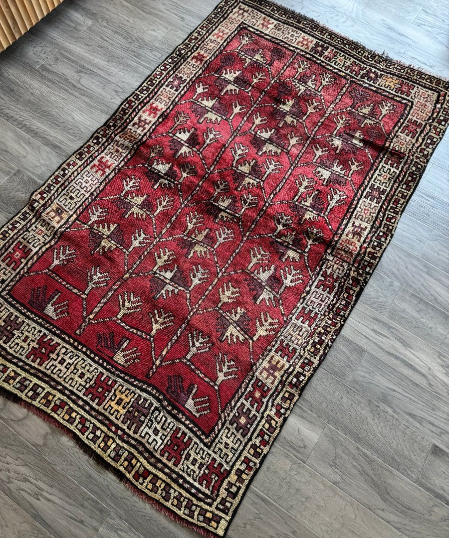 Red Persian rug with geometric border, repeating tree motifs and scattered animal figures