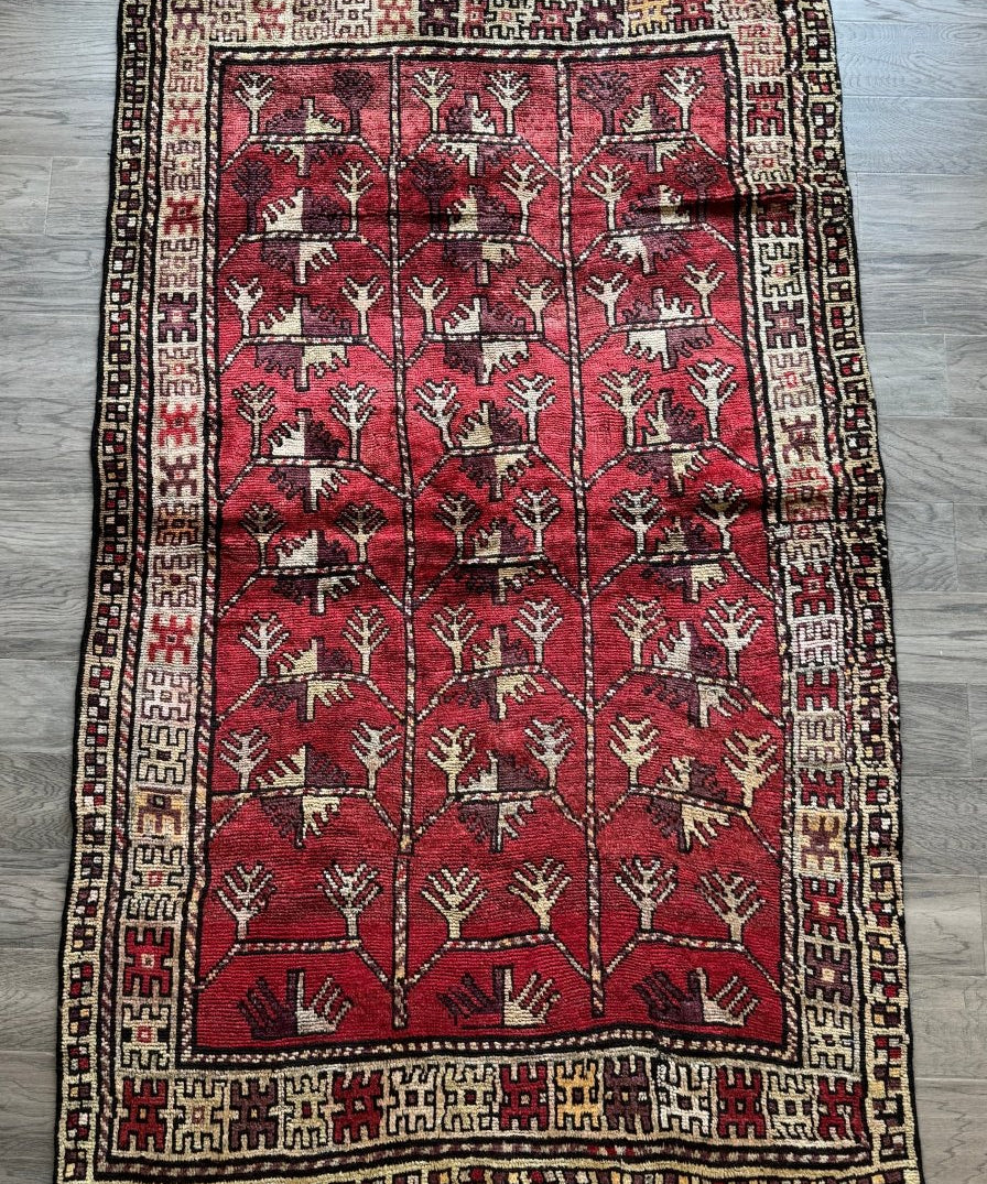 Red Persian rug with repeating tree motifs in rows, wide cream border and corner accents
