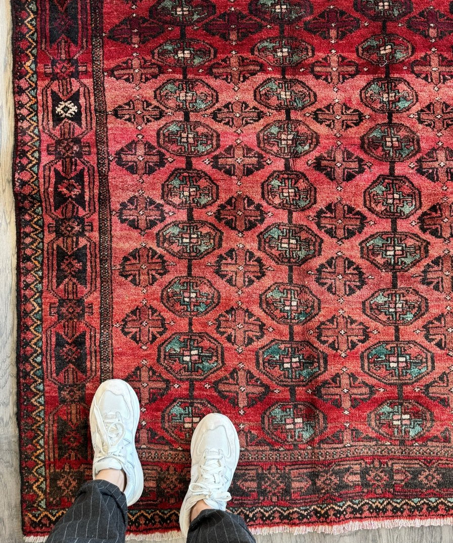 Red Persian Baluch rug with geometric medallions and patterned border edge.