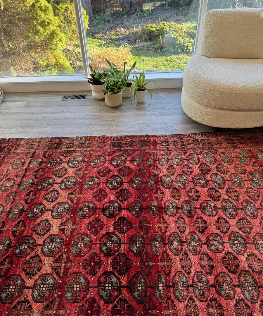 Red Persian Baluch rug with repeating geometric medallion pattern.