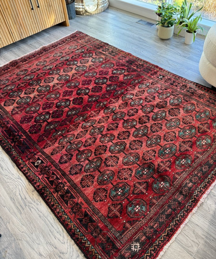 Red Persian Baluch rug with geometric medallions and dark striped fringe border.