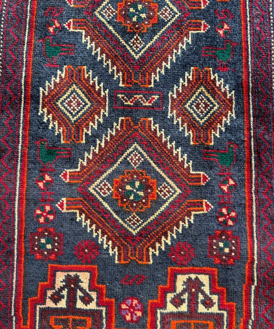Close-up of Persian Baluch runner rug pattern: dark navy field with red diamonds and accents.