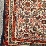 Persian Bidjar rug corner close-up with striped border and red, orange, and black motifs.