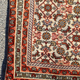 Persian Bidjar rug corner close-up with striped border and red, orange, and black motifs.