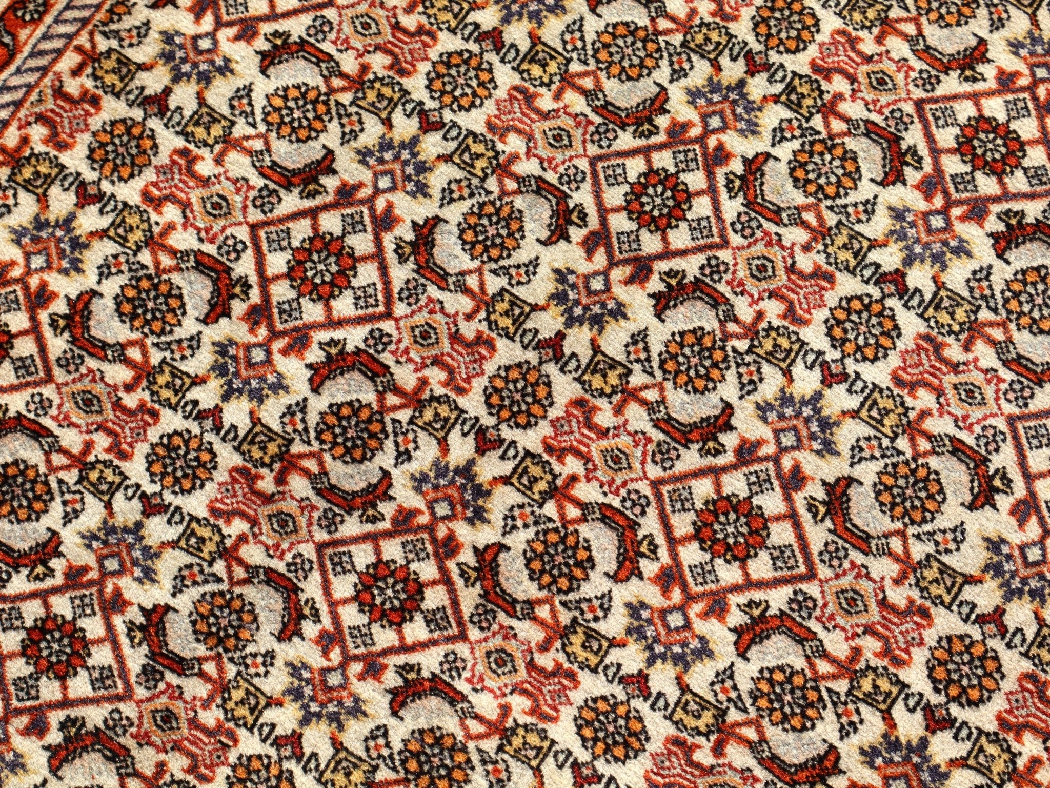 Persian Bidjar rug texture close-up with cream background and red-orange geometric motifs.
