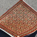 Persian Bidjar rug folded corner view showing cream field, red border, and patterned medallions.