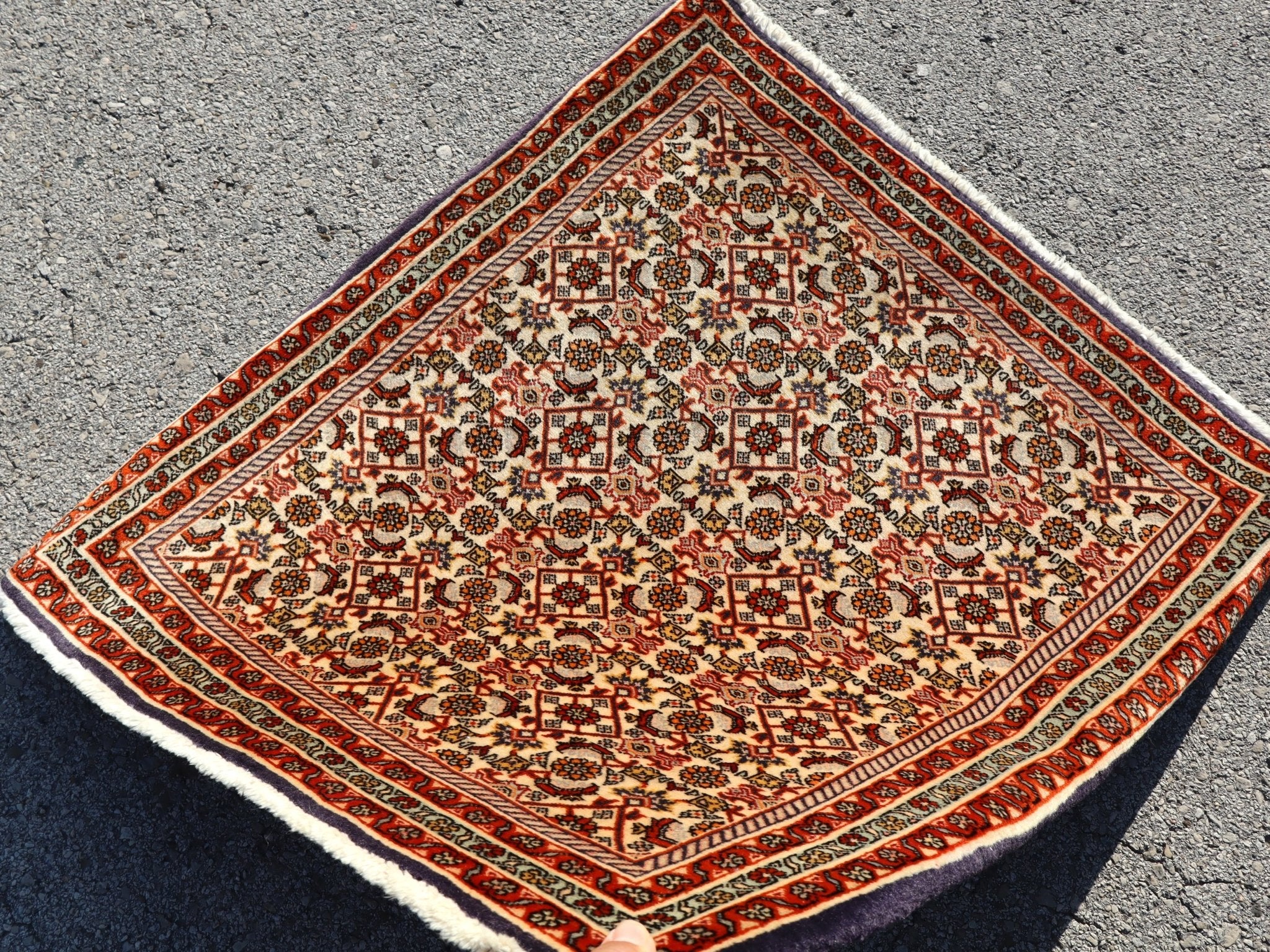 Persian Bidjar rug folded corner view showing cream field, red border, and patterned medallions.