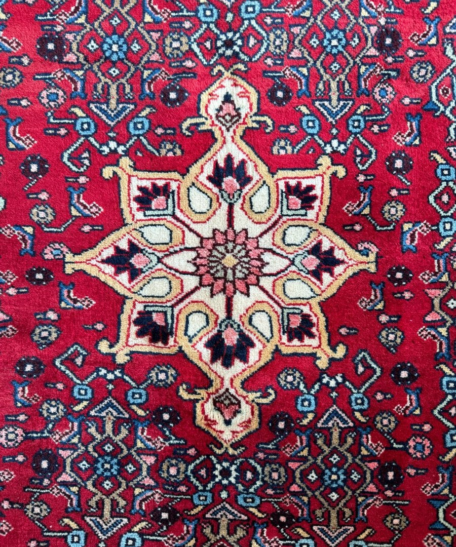 Persian Bidjar rug close-up showing red ground with blue diamond motifs and cream medallion.