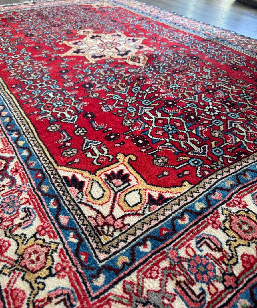 Persian Bidjar rug corner with red field, cream accents, and blue edge trim.
