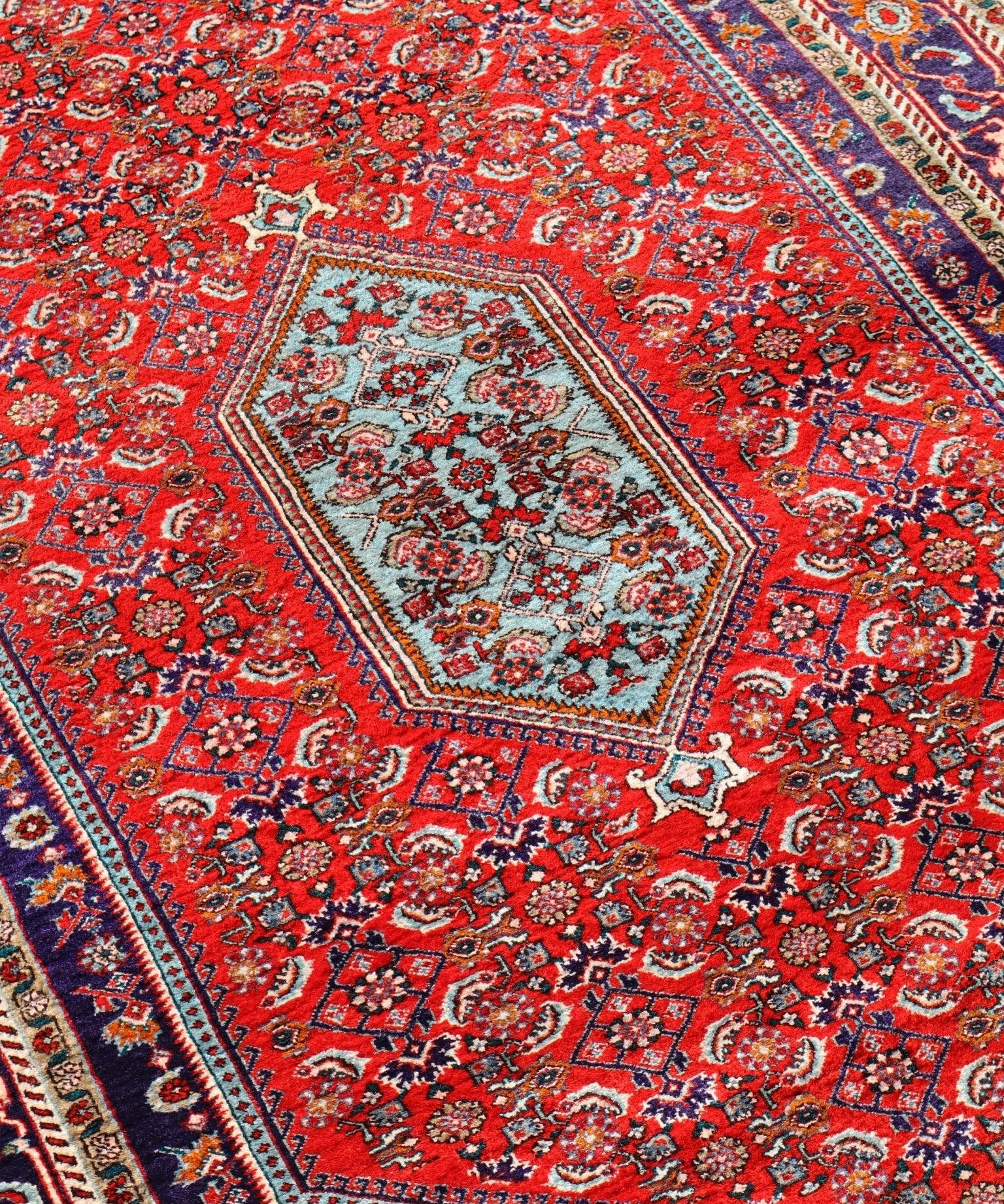 Rug close-up with red background, light medallion, and navy blue corner border