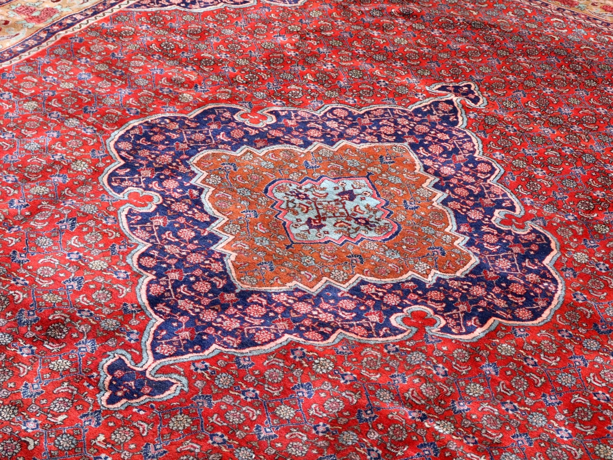 Persian rug central medallion with navy, orange, and red floral details across the field