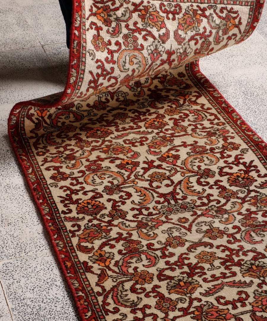Persian Bidjar runner rug close-up showing cream pile and red decorative motifs; rolled edge visible.