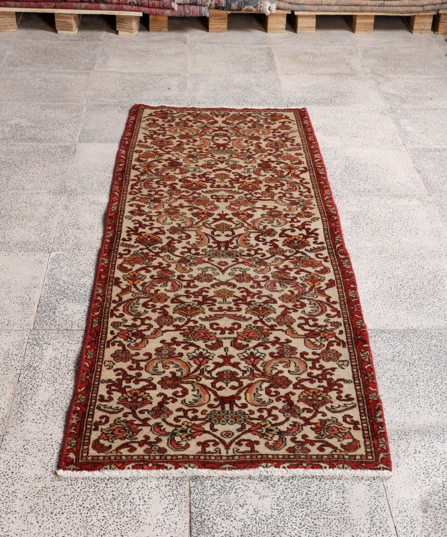 Persian Bidjar runner rug laid flat, cream base with red floral scrollwork and dark red edging.