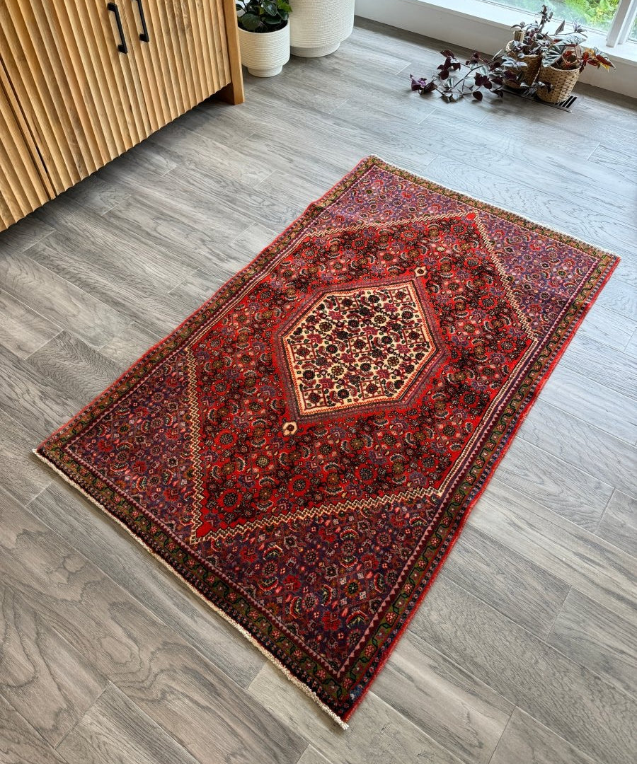 Persian Bijar rug with red field and central geometric medallion on light wood floor