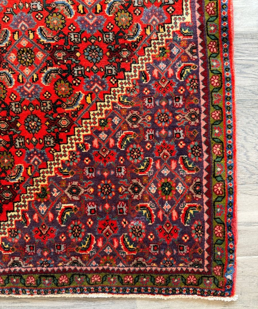 Persian Bijar rug close-up of red corner field with multicolor diamond motifs